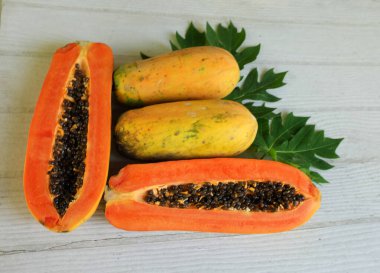 Üst ve düz bir şekilde olgun papaya meyveli papaya, yeşil yapraklı, yalıtılmış beyaz ahşap arka plan. Sağlıklı beslenme için sebze ve meyve.