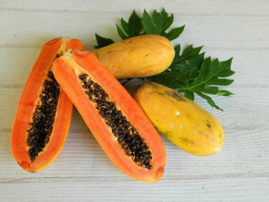 Üst ve düz bir şekilde olgun papaya meyveli papaya, yeşil yapraklı, yalıtılmış beyaz ahşap arka plan. Sağlıklı beslenme için sebze ve meyve.