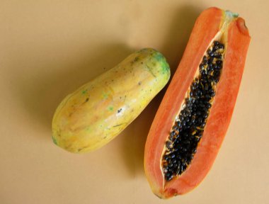 Üst ve düz bir zemin üzerinde yeşil yapraklı, dilimlenmiş, turuncu pastel bir zemin üzerinde tatlı olgun bir papaya meyvesi var. Sağlıklı beslenme için sebze ve meyve.