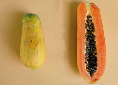 Üst ve düz bir zemin üzerinde yeşil yapraklı, dilimlenmiş, turuncu pastel bir zemin üzerinde tatlı olgun bir papaya meyvesi var. Sağlıklı beslenme için sebze ve meyve.