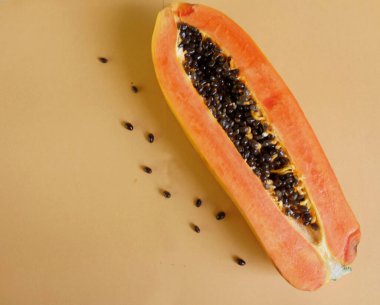 Üst ve düz bir zemin üzerinde yeşil yapraklı, dilimlenmiş, turuncu pastel bir zemin üzerinde tatlı olgun bir papaya meyvesi var. Sağlıklı beslenme için sebze ve meyve.