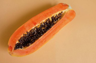 Üst ve düz bir zemin üzerinde yeşil yapraklı, dilimlenmiş, turuncu pastel bir zemin üzerinde tatlı olgun bir papaya meyvesi var. Sağlıklı beslenme için sebze ve meyve.