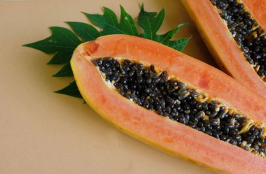 Üst ve düz bir zemin üzerinde yeşil yapraklı, dilimlenmiş, turuncu pastel bir zemin üzerinde tatlı olgun bir papaya meyvesi var. Sağlıklı beslenme için sebze ve meyve.