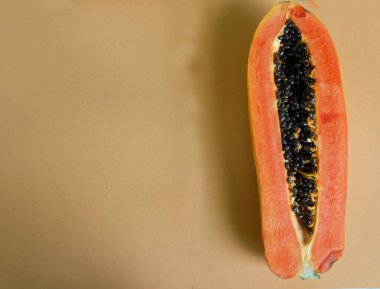 Üst ve düz bir zemin üzerinde yeşil yapraklı, dilimlenmiş, turuncu pastel bir zemin üzerinde tatlı olgun bir papaya meyvesi var. Sağlıklı beslenme için sebze ve meyve.