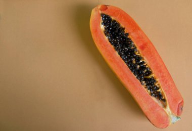 Üst ve düz bir zemin üzerinde yeşil yapraklı, dilimlenmiş, turuncu pastel bir zemin üzerinde tatlı olgun bir papaya meyvesi var. Sağlıklı beslenme için sebze ve meyve.
