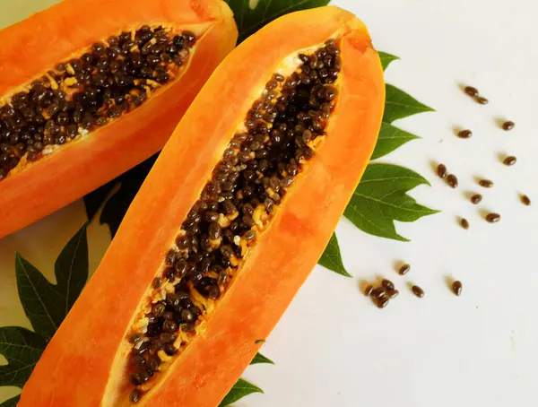 Üst ve düz taze, olgun bir papaya meyvesi uzanıyor. Tohumları, yemek dokusunu, kesimini, kesilmiş meyveleri beyaz bir zeminde izole edilmiş. Sağlıklı beslenme için sebze ve meyve