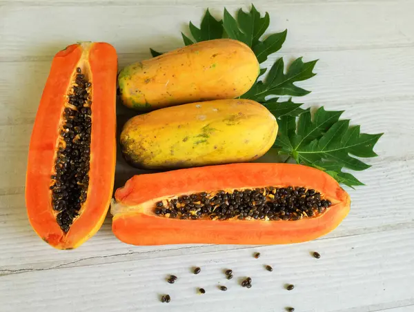 Üst ve düz bir şekilde olgun papaya meyveli papaya, yeşil yapraklı, yalıtılmış beyaz ahşap arka plan. Sağlıklı beslenme için sebze ve meyve.