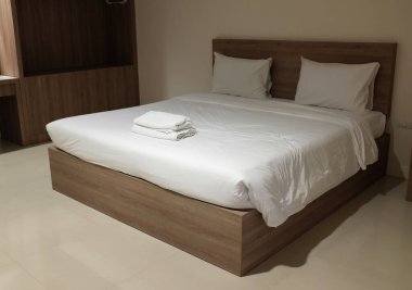 Yakından ve yandan bakınca lüks otel odası şık bir şekilde dekore edilmiş, geniş bir yatak, temiz, yumuşak beyaz çarşaf seti, beyaz havlular ve minimalist bir yatak başlığı olan geniş bir yatak..