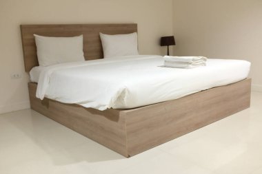 Yakından ve yandan bakınca lüks otel odası şık bir şekilde dekore edilmiş, geniş bir yatak, temiz, yumuşak beyaz çarşaf seti, beyaz havlular ve minimalist bir yatak başlığı olan geniş bir yatak..