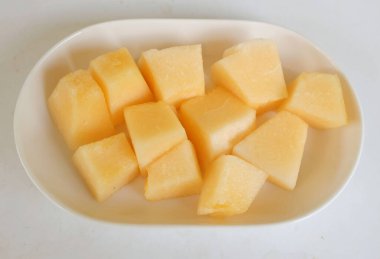 Olgun portakal sarısı yedi, sarı ballı kavun, altın karpuz parçalara ayrılmış ve beyaz seramik bir tabakta yemeye hazır beyaz bir zemin üzerinde izole edilmiş.