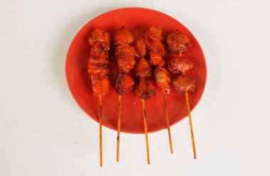 appetizing a chicken butt grilled ,chicken grilled skewered in a red ceramic plate on bamboo isolate on a white backdrop . halal food, street food in thailand