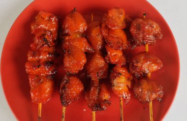 appetizing a chicken butt grilled ,chicken grilled skewered in a red ceramic plate on bamboo isolate on a white backdrop . halal food, street food in thailand