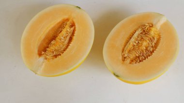 Olgun portakallı tatlı yedi, sarı ballı kavun, parçalanmış altın kavunlar, tohumlarla dilimlenmiş beyaz bir arka planda izole edilmiş.