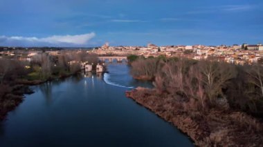 Duero Nehri boyunca ilerleyen hava aracı su değirmenlerinin yanından geçiyor ve taş köprüyü ve katedrali, Zamora, İspanya 'yı gösteriyor.