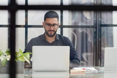 Siyah gömlekli genç adam ofiste telefonla konuşuyor.