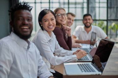 İş toplantısı sırasında dijital cihazların ve belgelerin yanında oturan çok kültürlü meslektaşlar