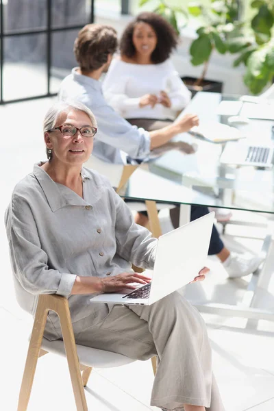 mature woman sitting with laptop looking at camera.