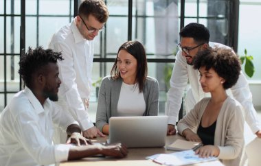 Çevrimiçi projeyi tartışan mutlu genç bayan çalışan, gözlüklü yetenekli takım liderine bilgisayar sunumu yapıyor. Uygulamaları kullanarak laptopta çift olarak çalışan dost canlısı meslektaşlar.