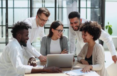 Çevrimiçi projeyi tartışan mutlu genç bayan çalışan, gözlüklü yetenekli takım liderine bilgisayar sunumu yapıyor. Uygulamaları kullanarak laptopta çift olarak çalışan dost canlısı meslektaşlar.