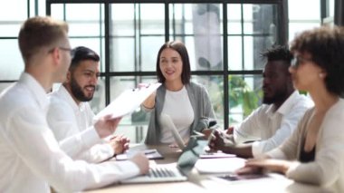 Çevrimiçi projeyi tartışan mutlu genç bayan çalışan, gözlüklü yetenekli takım liderine bilgisayar sunumu yapıyor. Uygulamaları kullanarak laptopta çift olarak çalışan dost canlısı meslektaşlar.