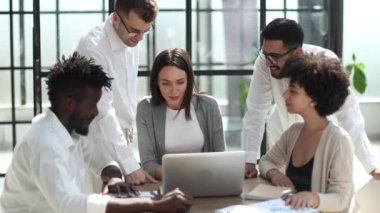 Çevrimiçi projeyi tartışan mutlu genç bayan çalışan, gözlüklü yetenekli takım liderine bilgisayar sunumu yapıyor. Uygulamaları kullanarak laptopta çift olarak çalışan dost canlısı meslektaşlar.