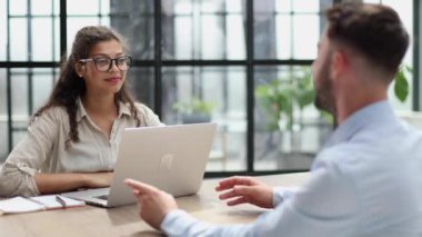 woman in glasses receives a client sitting at a laptop in the office