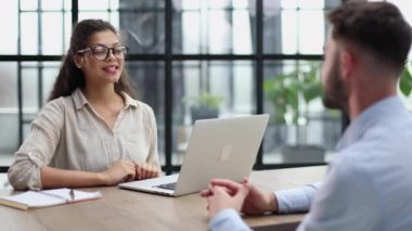 woman in glasses receives a client sitting at a laptop in the office