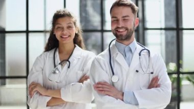 Two confident doctors standing in practice, with arms crossed