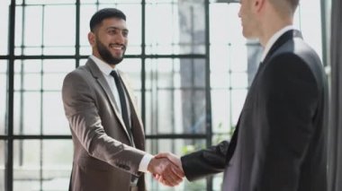 Two confident businessmen shaking hands and smiling while standing in the office