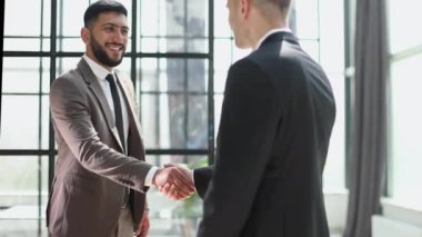 Two confident businessmen shaking hands and smiling while standing in the office
