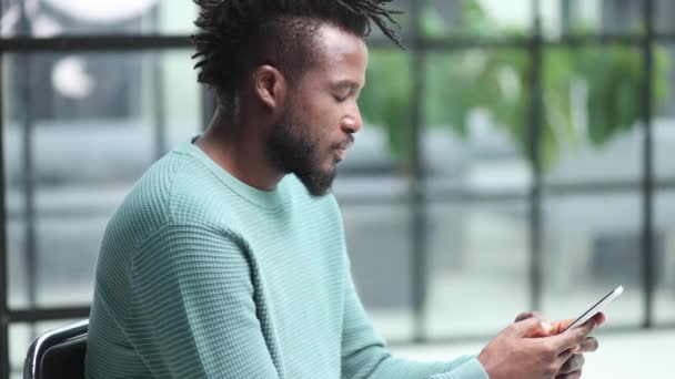 アフリカ系アメリカ人のビジネスマンが職場で携帯電話の企業アプリを使って — ストック動画