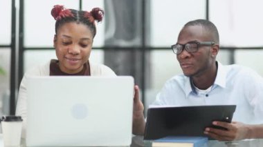 colleagues sitting together at a table in a modern office talking and using a laptop