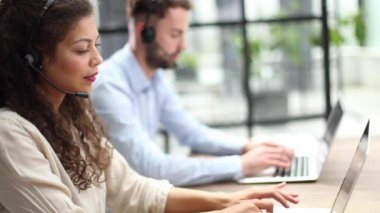 Neşeli bir kadın. Masa başında oturan, kulaklık takan bir öğretmen. Bilgisayardan yapılan konuşmalara bakıyor.