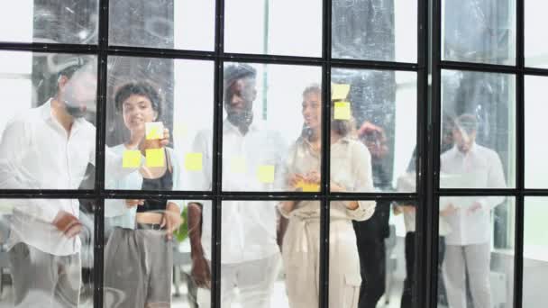通过在团队中工作来确保成功 年轻的现代人穿着雅致的休闲装 站在会议室的玻璃墙后面 用粘贴的字条写着 — 图库视频影像