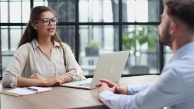 woman in glasses receives a client sitting at a laptop in the office