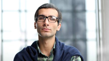 Gözlüklü bir adam kameraya ciddi bir ifadeyle bakıyor. Kafası ve omuzları yakın portrede.