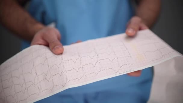 Freundlicher Arzt Schaut Auf Kardiogramm Auf Grauem Hintergrund — Stockvideo