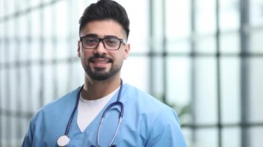 Hastanede kameraya poz veren genç bir erkek doktor.