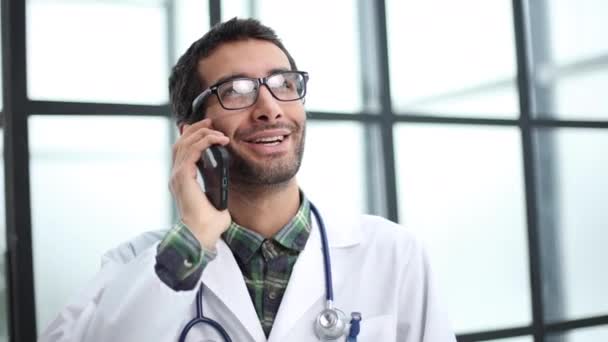 男性医師は病院で彼のオフィスで電話健康相談をしてる — ストック動画