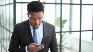 Genç Afrikalı Amerikalı adam akıllı telefonu elinde tutuyor, mesaj yazıyor, sosyal ağlarda arkadaşlarıyla sohbet ediyor.,