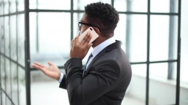 Ofiste cep telefonuyla konuşan gülümseyen Afrikalı genç bir adamın yakın plan portresi meslektaşlarının arka planına karşı.