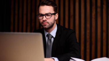 Modern bir ofisteki masasında bilgisayar kullanan genç bir iş adamının fotoğrafı..