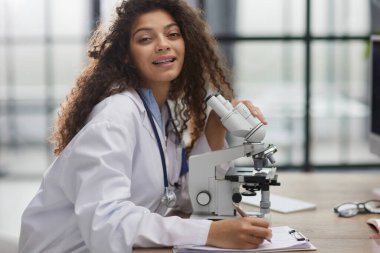 Çekici kadın bilim adamı mikroskoptan bakıyor.