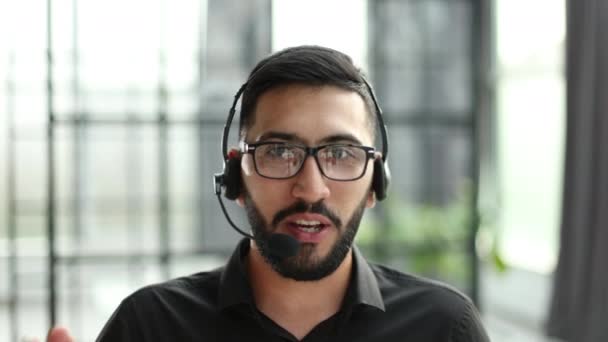集中されたビジネスマンのテレマーケティング担当者は 無線ヘッドセットを着用会議ビデオ通話は コンピュータ上のオンラインクライアントを相談します カスタマーケアサポートオフィスで男性のヘルプラインオペレーターの仕事 — ストック動画