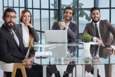 Ofis günleri. Bir grup iş adamı bir masada oturup kameraya bakıyorlar.