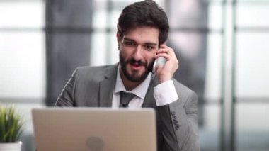 Ofiste bilgisayarla telefonla konuşurken gülümseyen adam.