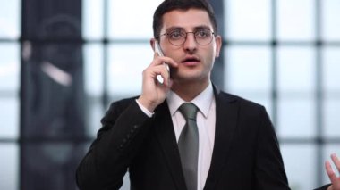 Yes, my business is doing well. a businessman talking on his cellphone while standing in his office.