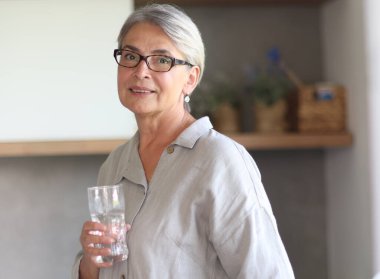 mature woman smiling close up in the office holding a glass of water