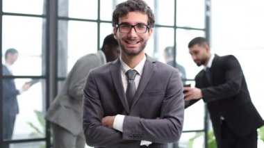 Genç Güvenilir İş Adamı, İş Arkadaşlarına Karşı Göğüs Üzerinden Koluyla Kameraya Gülümsüyor.