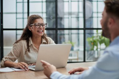 Masada oturan gözlüklü müdürün ofiste kameraya bakan bir müşterisi var.